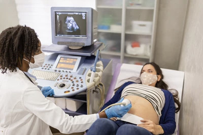 A technician in a lab coat is shown conducting an ultrasound on a pregnant woman, with the sonogram being displayed on a screen.