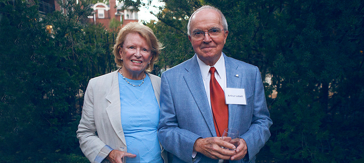 Sonia and Arthur Labatt are shown smiling outdoors, in front of greenery, while standing close together in business formal wear.