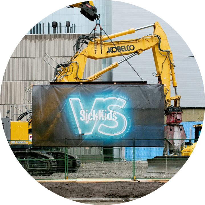 Construction equipment shown in the background, with a SickKids vs banner shown in the foreground, hung over newly broken ground.