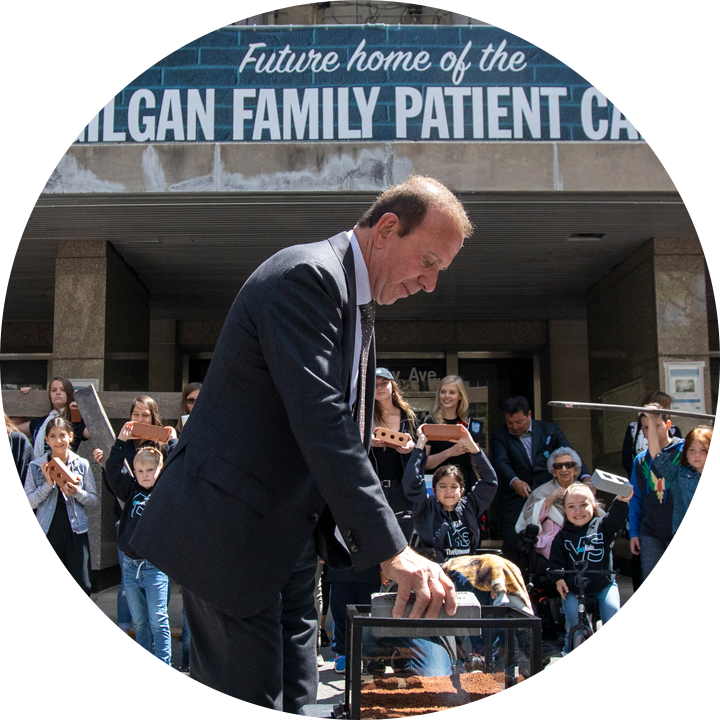 SickKids donor, Peter Gilgan, placing the symbolic first brick into a glass box, in front of SickKid Ambassadors, also holding bricks as they stand in front of the future home of the Peter Gilgan Family Patient Care Tower.