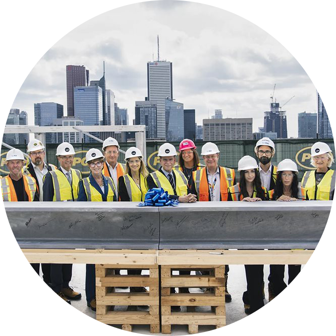 A group of people in hard hats and high visibility vests standing behind a large metal girder, on the roof of the new Patient Support Centre.