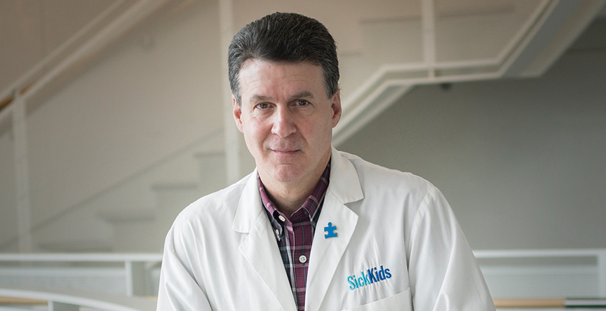 Dr. Stephen Scherer, Chief of Research at SickKids Research Institute, smiling at the camera, while leaning on a balcony in the Research Institute.