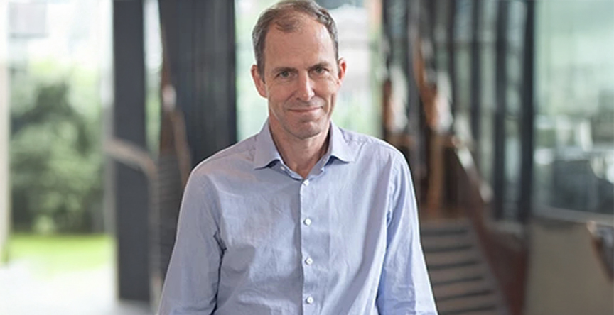 Dr. Peter Dirks stands inside a glass building with his hands on a railing.