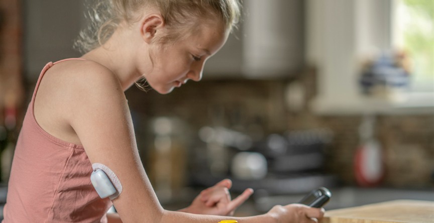 Teen girl wearing a glucose monitor checks her blood sugar