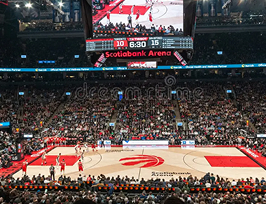 A basketball court in an arena with the Toronto Raptors logo, surrounded by a crowd of sports fans